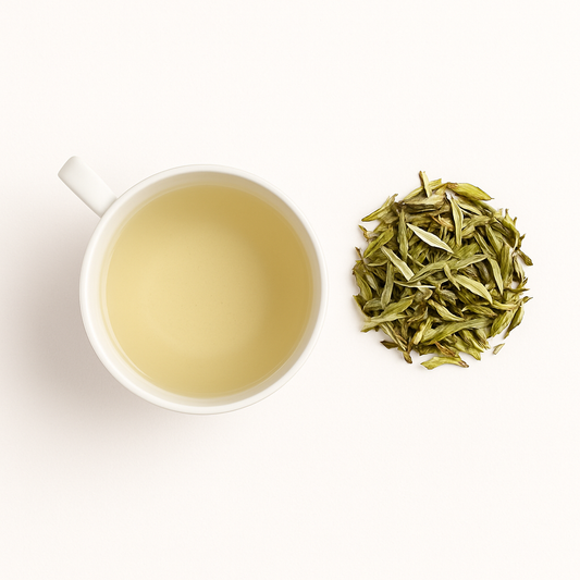 Delicate white tea infusion in a clear cup surrounded by white tea leaves; skin-protective antioxidant tea with gentle energy