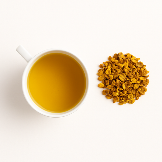 Golden-hued cup of turmeric and ginger tea with scattered roots; anti-inflammatory tea for radiant, calm skin
