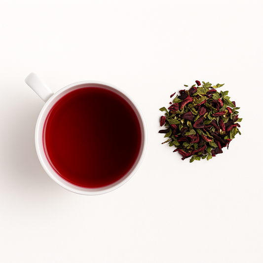 Glass cup of BloomBlend hibiscus and peppermint tea beside loose leaves; vibrant herbal tea for skin clarity and anti-inflammatory benefits
